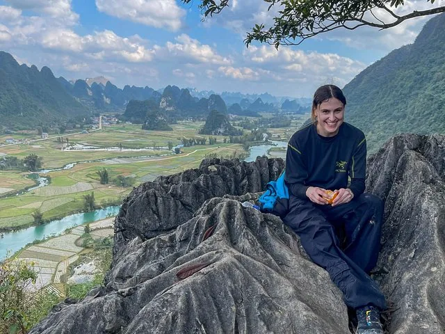 Woman sitting on rocky outcrop overlooking a vast valley with river.