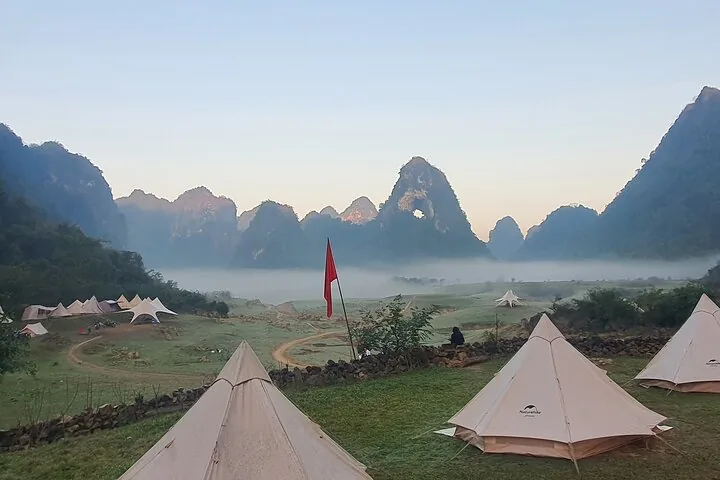 Camping tents pitched in a valley with karst mountains and morning mist.