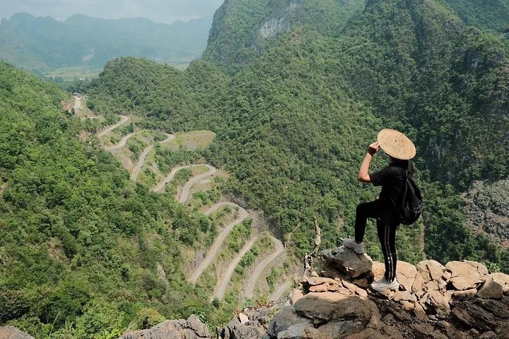Hiker looking at a winding mountain road from a rocky viewpoint.